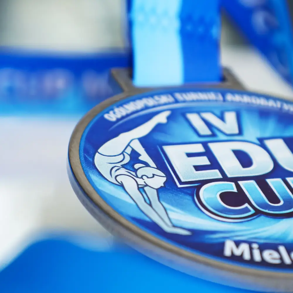 Zbliżenie pod kątem na pamiątkowy medal akrobatyczny z Mielca, ukazujące przestrzenną strukturę nadruku UV oraz dwukolorową, niebieską wstęgę.