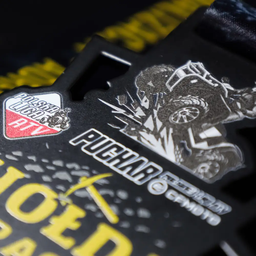 Zbliżenie pod kątem na surowy medal Hołda Race z wyraźnym, żółtym napisem, symbolem górniczego kilofa oraz kolorowym logo Polska Liga ATV.